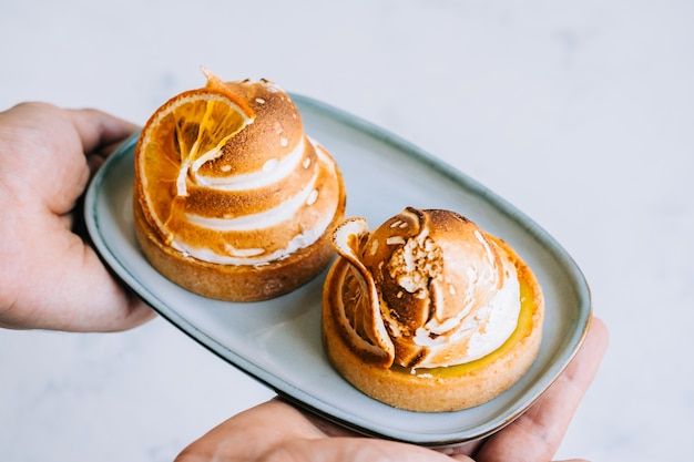 Postre de tartaleta de limón con merengue en un plato en las manos.