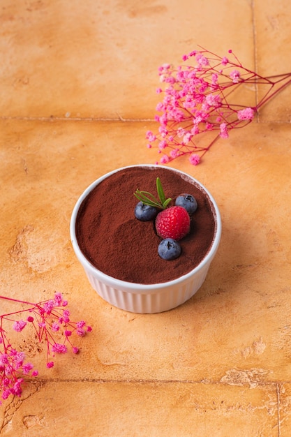 Postre tiramisú con frutos rojos sobre fondo marrón con flores rosadas foto de alta calidad