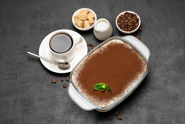 Postre tiramisú italiano tradicional en una fuente para hornear de vidrio y una taza de café espresso caliente fresco sobre fondo de hormigón o mesa