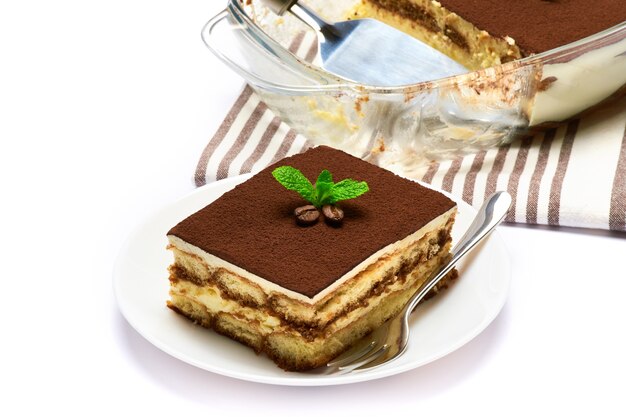 Postre tiramisú italiano tradicional en porción de plato para hornear de vidrio en placa y escápula aislado en blanco