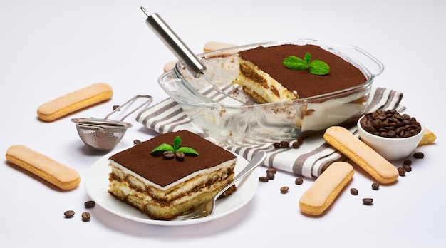 Postre tiramisú italiano tradicional en porción de plato para hornear de vidrio en placa y escápula aislado en blanco