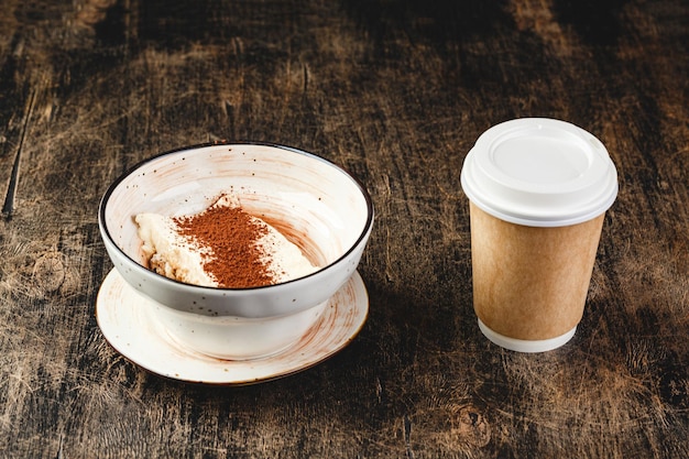 Postre tiramisú en tazón y vaso de papel desechable para beber en mesa de madera