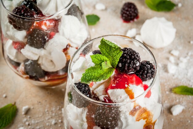 Postre tradicional inglés. Eton mess: crema batida, merengue, moras frescas, salsa y caramelo. En servir vasos en una mesa de piedra clara. Copia espacio