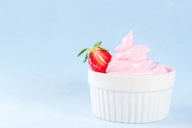 Postre de verano de dieta saludable, yogurt helado de vainilla y bayas o helado suave en tazones blancos, aislado sobre fondo azul claro