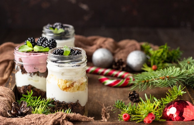 Postres en capas con pastel, crema batida y moras sobre fondo de Navidad