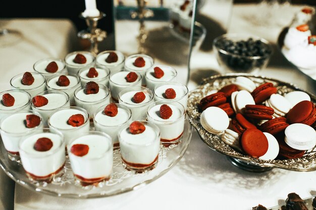 Postres de crema fría en vasos de pie junto a plato de plata con macarrones