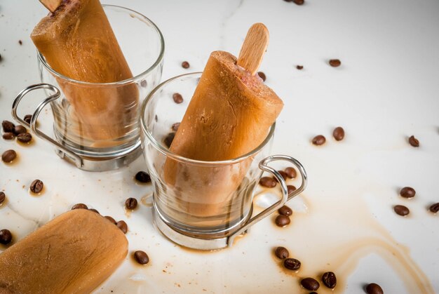 Postres de verano. Bebidas congeladas Paletas dulces hechas de café y leche. En tazas de café, en una mesa de mármol blanco, con granos de café.