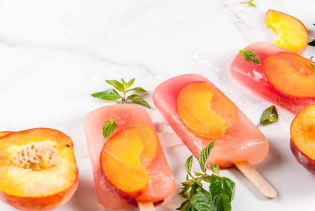 Postres de verano. Bebidas congeladas Paletas de fruta dulce de té de durazno congelado con menta. Sobre una mesa de mármol blanco, con ingredientes duraznos, menta, hielo.