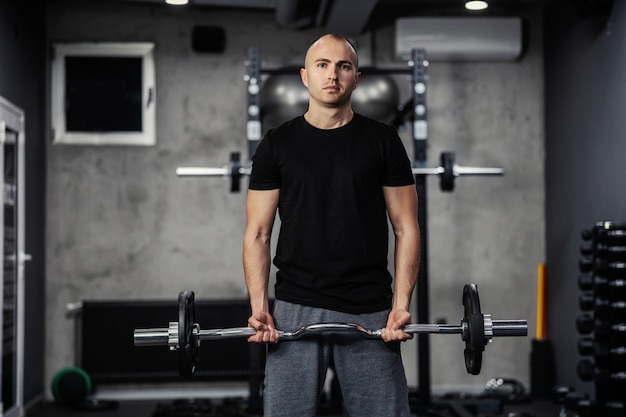 Postura adecuada antes de realizar ejercicios. Un hombre en ropa deportiva bombea los músculos de su brazo y levanta una barra con el plato de pesas con ambas manos en un gimnasio moderno. Un primer plano de una persona del sexo masculino