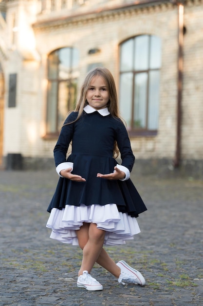 Postura de estilo plie. A pequena bailarina usa uniforme escolar. Dançarina de balé pequena ao ar livre. Escola de balé. Educação em dança. De volta à moda da escola. Código de vestimenta formal. Explore o mundo da dança.