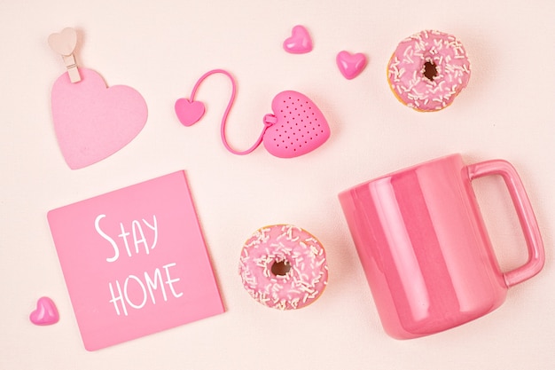 Postura plana com acessórios rosa, xícara de chá e donuts sobre parede rosa claro. Vista do topo. Rituais matinais, conceito de ficar em casa