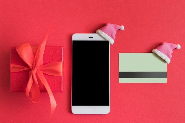 Postura plana com caixa de presente de Natal, smartphone e cartão de crédito com chapéu de Papai Noel no vermelho