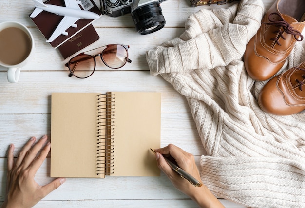 Postura plana com mão escrevendo no caderno, roupa quente de conforto para o tempo frio, acessórios de viagem. outono confortável, estilo no conceito de cores de tom de terra, vista superior, copie o espaço