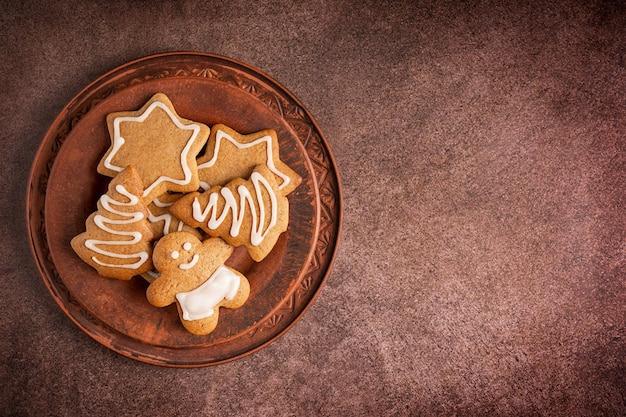 Postura plana com prato de biscoitos de gengibre picantes caseiros decorados com glacê branco na mesa marrom