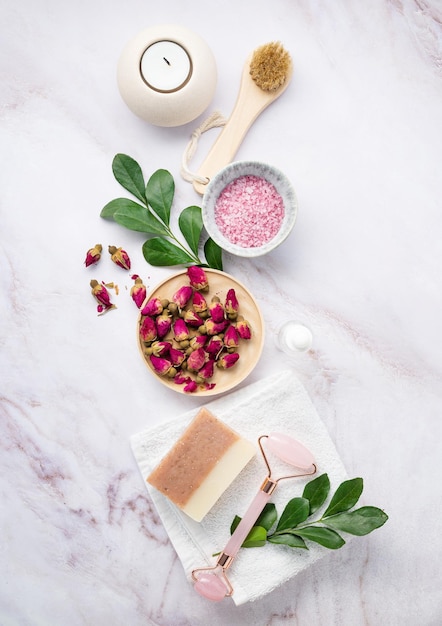 Postura plana com sal marinho orgânico com escova de vela de sabão de flores rosas secas e gua sha em um fundo de mármore rosa O conceito de um produto de spa natural Vista superior Orientação vertical