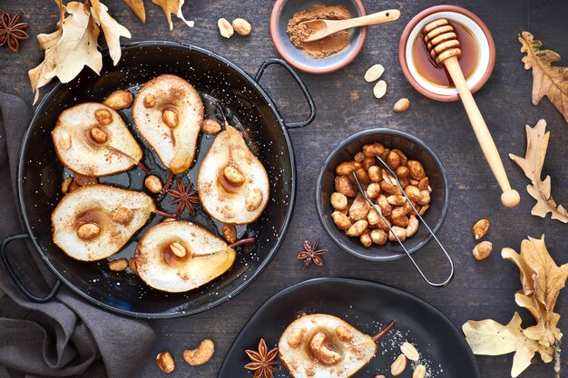 Postura plana com uma bandeja de peras assadas com nozes caramelizadas na mesa de madeira escura com folhas de outono