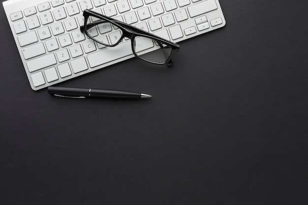 Foto postura plana da área de trabalho com óculos e teclado