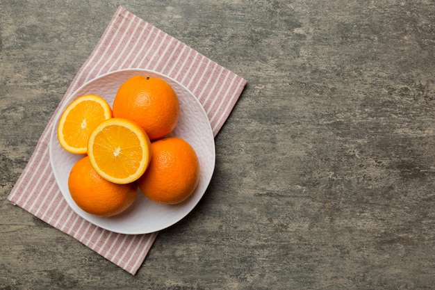 Postura plana de frutas frescas de laranja com fatias em prato sobre fundo colorido vista superior com espaço de cópia