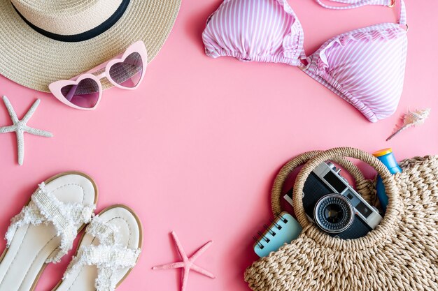 Postura plana de itens de verão com biquíni rosa pastel, chapéu de praia, chinelo, bolsa, câmera, protetor solar, notebook e óculos de sol, vista superior e espaço de cópia. conceito de verão.