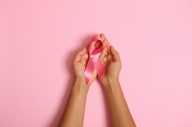 Postura plana de mãos segurando uma fita rosa em fundo rosa, conscientização do câncer de mama, dia rosa de outubro, World Wancer Way, sobrevivente de câncer nacional Say. Cuidados de saúde da mulher e conceito médico. Copie o espaço