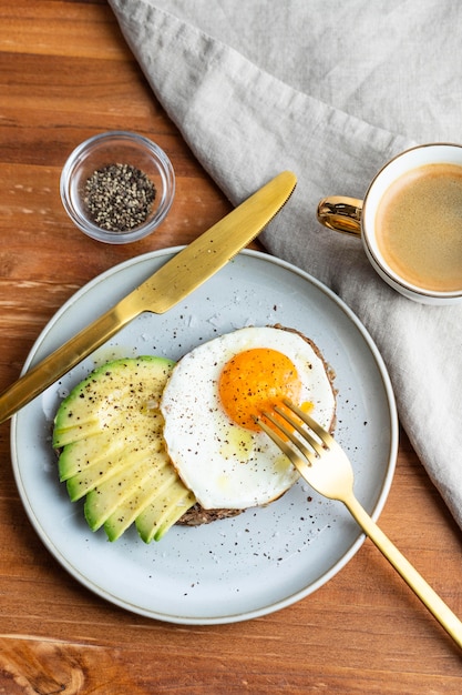 Foto postura plana de ovo frito de café da manhã no prato com torrada de abacate e café