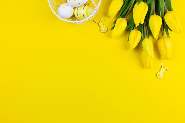 Postura plana de páscoa com tulipas amarelas ovos de páscoa coloridos e decoração de coelhinhos em fundo amarelo Vista superior Copiar espaço