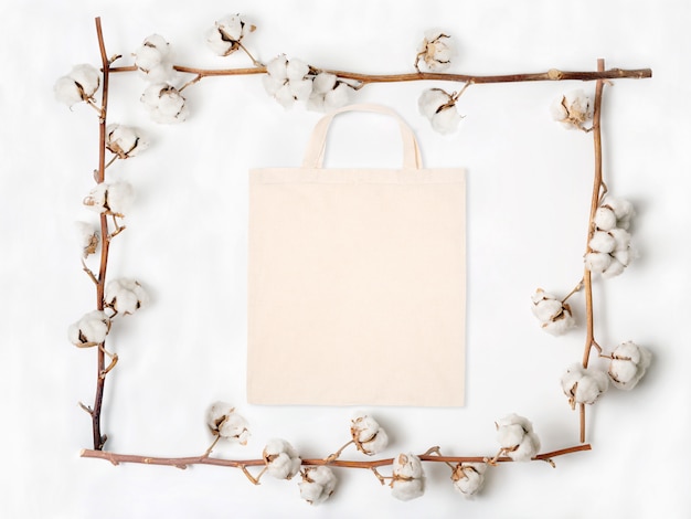 Postura plana de saco de tecido em branco com galhos de flores de algodão no fundo branco