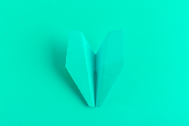 Postura plana de um avião de papel sobre fundo verde cor pastel