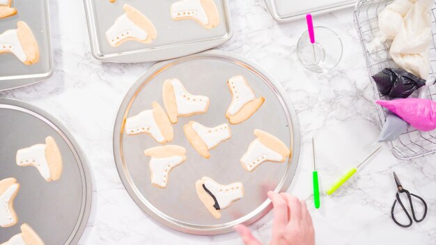 Postura plana. Decorando biscoitos de açúcar em forma de patins de gelo com glacê real de cor preta.