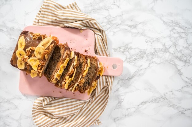 Postura plana. Fatias de pão de banana e nozes regadas com caramelo caseiro em uma tábua de corte rosa.