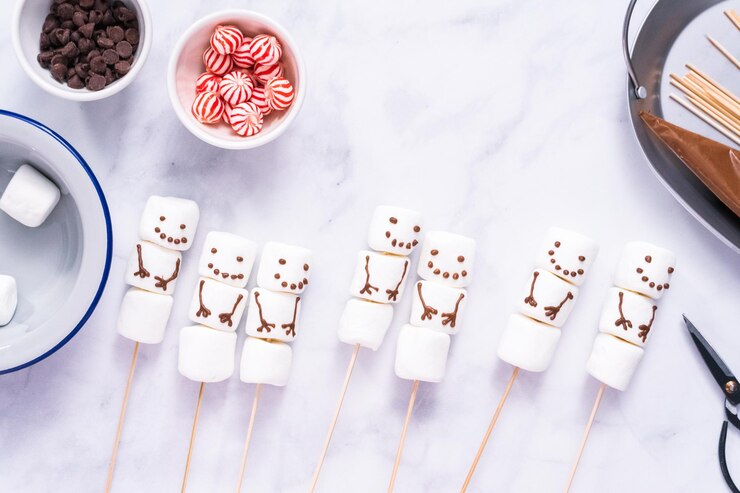 Foto postura plana. fazendo bonecos de neve de marshmallow e renas em palitos para chocolate quente e bebidas de cacau.