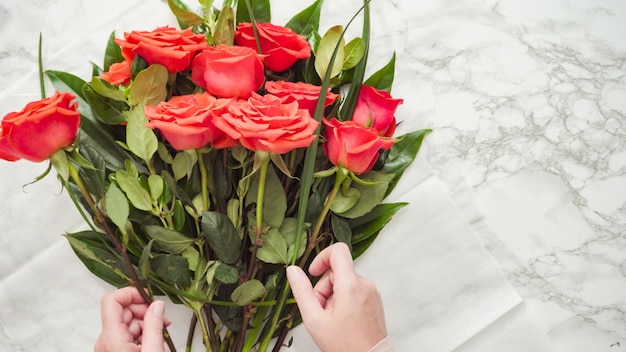 Postura plana. Florista embrulhando rosas vermelhas em um lindo buquê.