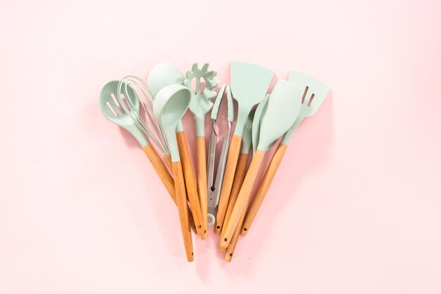 Postura plana. Novos utensílios de cozinha de silicone azul com alças de madeira em um fundo rosa.