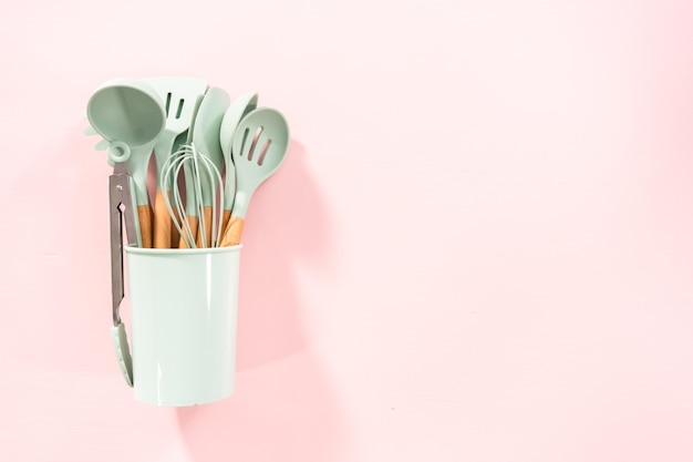 Postura plana. Novos utensílios de cozinha de silicone azul com cabos de madeira em um fundo rosa.