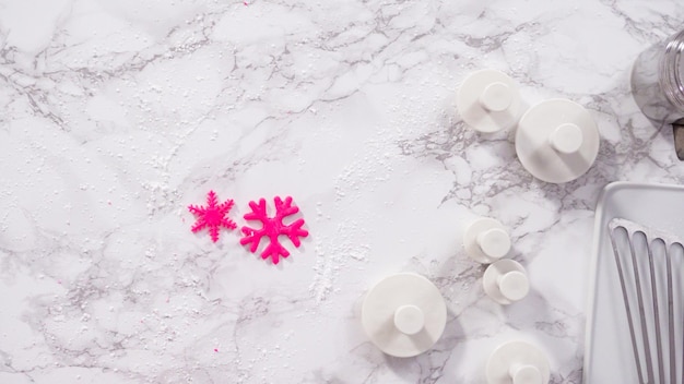 Postura plana. Passo a passo. Cortar flocos de neve com cortadores de biscoito de fondant rosa em um balcão de mármore.