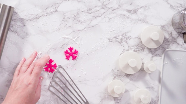 Postura plana. Passo a passo. Cortar flocos de neve com cortadores de biscoito de fondant rosa em um balcão de mármore.