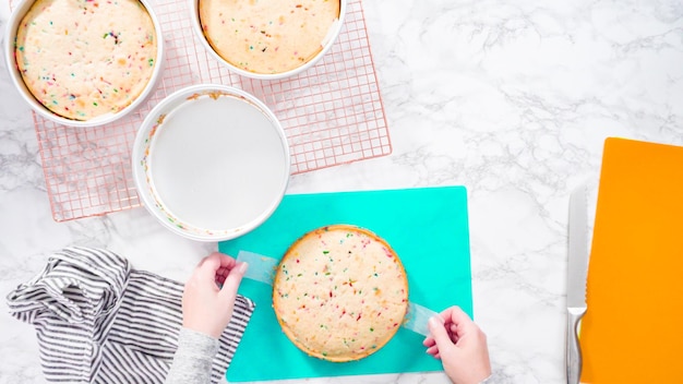 Postura plana. passo a passo. embrulhar bolo funfetti recém-assado em celofane e papel alumínio para armazenamento no freezer.