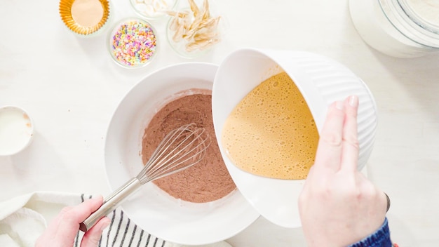 Postura plana. Passo a passo. Misturar os ingredientes em uma tigela branca para fazer cupcakes de chocolate unicórnio com cobertura de creme de manteiga.