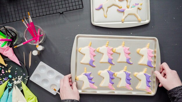 Postura plana. Passo a passo. Pintar glitter de comida em cima de biscoitos de açúcar de unicórnio com glacê real.