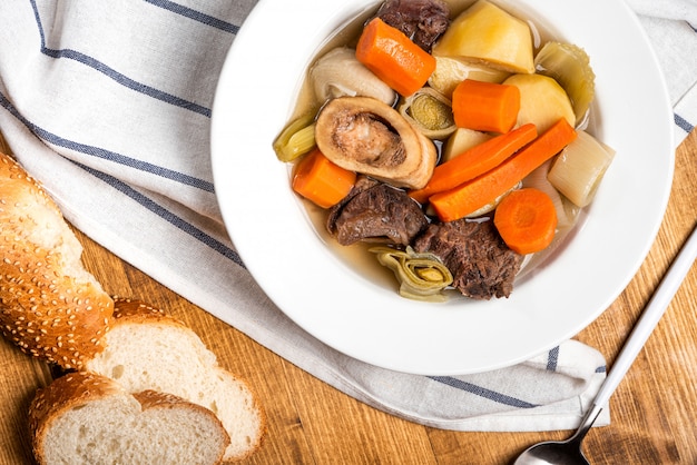 Foto pot-au-feu beliebte warme gerichte der traditionellen französischen küche. gedünstetes rindfleisch und gemüse mit rinderbrühe in einer weißen platte auf einem holztisch. warme wintermahlzeit.