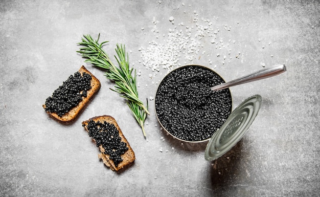 Pote com caviar preto e sanduíches na mesa de pedra