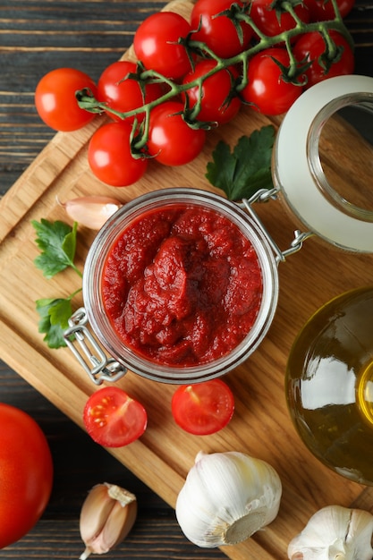 Pote com pasta de tomate na mesa de madeira com ingredientes