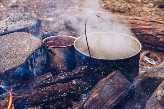 Pote de acampamento em chamas com café e água quente para chá ou ensopado. Alimentos fumegantes ao ar livre. Estilo de vida da vida selvagem cozinhando uma refeição deliciosa, foto de estoque Copyspace