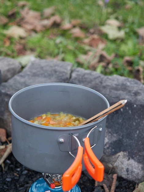 Pote de conceito de refeição de inverno ao ar livre de sopa de legumes no fogão a gás de acampamento ao ar livre