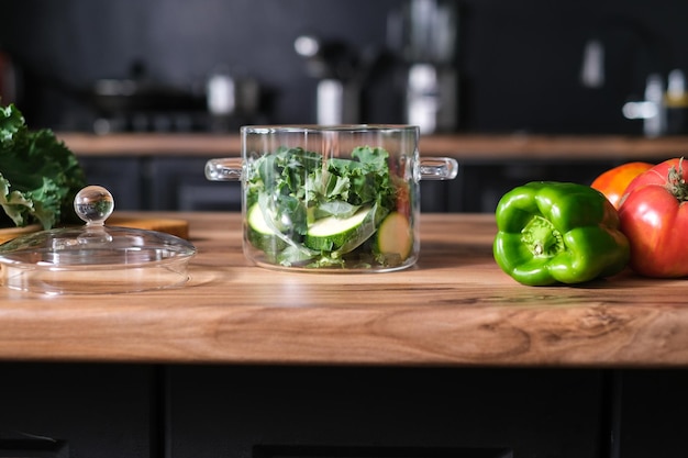 Pote de vidro elegante com legumes verdes na mesa da cozinha.