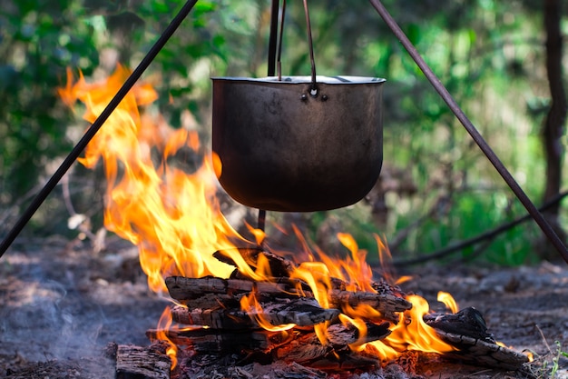 Pote turístico pendurado sobre o fogo em um tripé. Cozinhando na campanha.