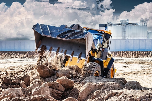 Potente excavadora o cargadora mueve la tierra en el sitio de construcción contra el cielo Una máquina de movimiento de tierras está nivelando el sitio Construcción de equipo pesado para movimiento de tierras