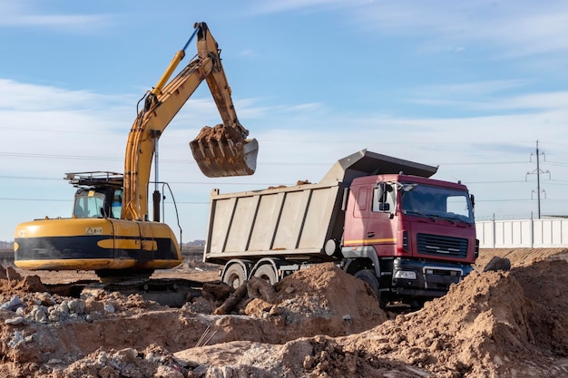 Una potente excavadora sobre orugas carga la tierra en un camión volquete contra el cielo azul Desarrollo y remoción de suelo del sitio de construcción