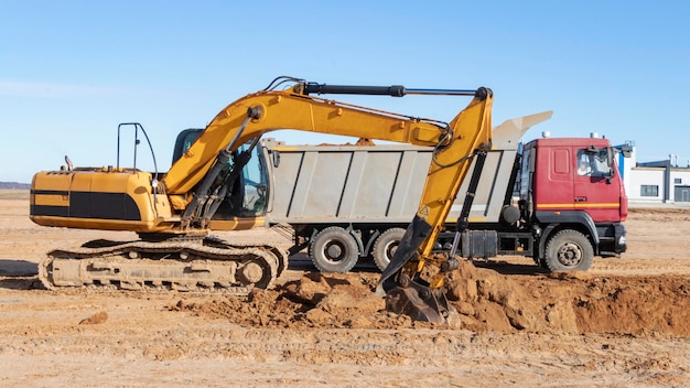 Una potente excavadora sobre orugas carga la tierra en un camión volquete contra el cielo azul Desarrollo y remoción de suelo del sitio de construcción