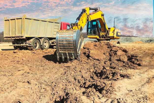 Una potente excavadora sobre orugas carga la tierra en un camión volquete contra el cielo azul Desarrollo y remoción de suelo del sitio de construcción